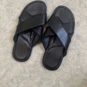 Svarta sandaler från Aldo - Snygga svarta sandaler från Aldo med korsade remmar. Perfekta för en avslappnad stil. Sulan har ett rutmönster för extra grepp.