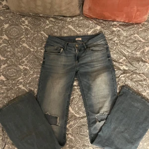 Blå jeans med slitningar från Nelly - Snygga blå jeans från Nelly med slitningar på knäna. De har en bootcut-stil och är tillverkade i jeansmaterial. Perfekta för en avslappnad look.