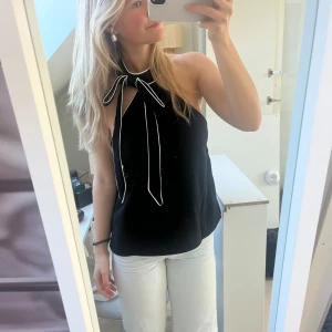Svart halterneck topp med knytband - Snygg svart halterneck topp med vita detaljer och knytband vid halsen.
