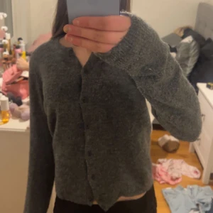 Grå stickad kofta - Mysig grå stickad kofta med knappar framtill. Perfekt för kyligare dagar och ger en avslappnad look. Långärmad design som håller dig varm och bekväm.