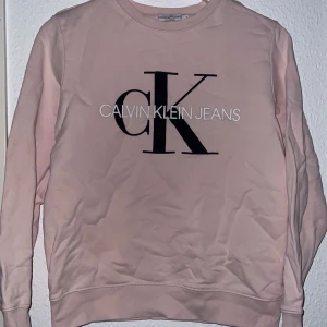 Rosa sweatshirt från Calvin Klein - Säljer en snygg rosa sweatshirt från Calvin Klein Jeans med deras ikoniska logga tryckt på framsidan. Tröjan har långa ärmar och en rund halsringning. Perfekt för en avslappnad stil. 🌸