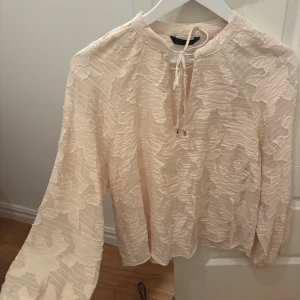 Beige blus med struktur från ZARA - Ny utan prislapp!! Beige blus från ZARA med transparent struktur och stora blommiga detaljer. Vida ärmar med resår vid handlederna och knytning i halsen som man knyter själv. 