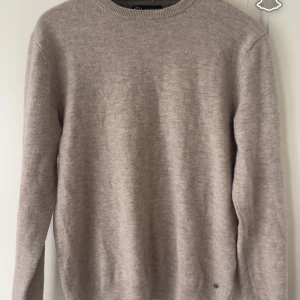 Beige stickad tröja från Lagency - Säljer en stilren beige stickad tröja från Lagency i storlek M. Tröjan har rund halsringning och långa ärmar, perfekt för dig som gillar enkel och clean look. Materialet är mjukt och skönt, passar dig som vill ha en klassisk vibe i garderoben gjord i Marino ull.