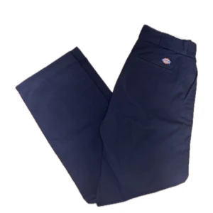 Svarta Dickies byxor W26 - Klassiska svarta byxor från Dickies i rak modell. Byxorna har en enkel design med Dickies-logga ovanför bakfickan och är tillverkade i ett slitstarkt bomullsmaterial. Perfekta för en clean och tidlös streetstil.