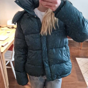Mörkgrön pufferjacka med huva - Säljer en mörkgrön pufferjacka med stor huva, perfekt till kalla vinterdagar! Väldigt fint skick, från bikbok i strl s