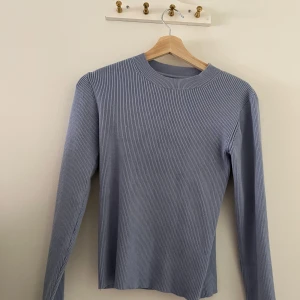 Ljusblå ribbad tröja från Å Woman - Supersnygg ljusblå ribbad tröja från Å Woman. Tröjan har lång ärm, rund halsringning och är tillverkad i ett mjukt, stretchigt material som sitter skönt på kroppen. Perfekt att styla med jeans eller kjol för en clean look. Nypris 400kr rabatterad till 347kr och mitt pris 260kr