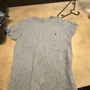 Blå t-shirt från Polo Ralph Lauren - Snygg ljusblå t-shirt från Polo Ralph Lauren med klassisk passform. T-shirten har korta ärmar, rund halsringning och en liten bröstficka med broderad logga. Tillverkad i mjuk bomull som känns skön mot huden. Perfekt till jeans eller shorts.