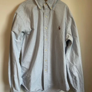 Randig skjorta från Ralph Lauren - Klassisk slim fit skjorta från Ralph Lauren i blåvitt randigt mönster. Skjortan är i super bra skick då den knappast är använd, nypris = 2000 kr mitt = 349 kr, skriv om minsta lilla fundering!