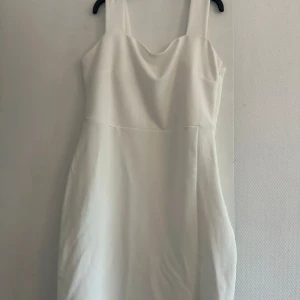 Vit kort klänning från Amisu - Snygg vit kort klänning från Amisu med breda axelband och en liten slits framtill. Klänningen har en enkel och stilren design med lätt drapering vid bysten. Perfekt för dig som gillar en clean och fräsch look.