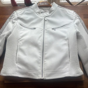 Vit skinnjacka från FB Sister XL - Säljer en snygg vit skinnjacka från FB Sister i storlek XL. (Stl 40/42) Jackan har coola detaljer med dragkedjor framtill, ståkrage med tryckknapp och ribbade partier på sidor och ärmar. Perfekt för dig som vill sticka ut med en fräsch look. Jackan har några fläckar på insidan, förstora upp. Knappt använd. Liten skada på framsidan se bild ca. 1mm stor. Djur finns i hemmet 