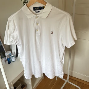 Vit Polo Ralph Lauren t-shirt M - Vit t-shirt från Polo Ralph Lauren i slim fit med klassisk krage och tre knappar framtill. Ikonisk broderad logga med polospelare på bröstet. Tillverkad i mjuk bomull, perfekt för en clean och stilren look. Storlek medium herr. Ny pris ca 1500kr