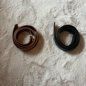 Två stilrena bälten i skinn - Säljer två klassiska bälten i skinn – ett brunt med silverfärgat spänne och ett svart med vit söm. Båda är raka och smala, perfekta för att lyfta din outfit med en clean look. Passar lika bra till jeans som till kostymbyxor.