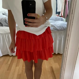 Röd volangig bandeau tubtopp och kjol  - Det är en kjol men kan ha den som topp. Säljer en superfin röd bandeau tubtopp med flera lager volanger. Toppen är axelbandslös och har en luftig, plisserad look som verkligen sticker ut. Perfekt att styla med både jeans och kjol för en trendig vibe. 