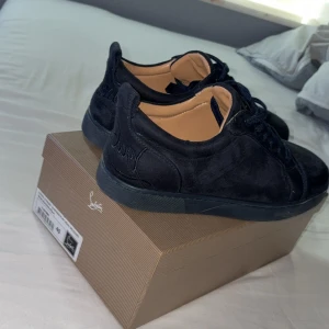 Navy sneakers från Christian Louboutin - Säljer ett par navy sneakers från Christian Louboutin i mocka med klassisk röd sula och snygga snördetaljer. Skorna har rund tå och diskret broderad logga på sidan. Insidan är i beige skinn och sulan har den ikoniska röda signaturen.