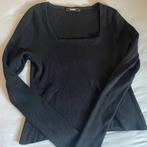 Svart ribbad topp från BikBok - Svart långärmad topp från BikBok med fyrkantig ringning och ribbade detaljer nedtill och på ärmarna. Snygg och enkel modell som passar till många olika outfits. Mjuk och stretchig, perfekt för dig som gillar stilrena plagg.