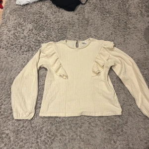 Beige blus med volang från Zara - Supersöt beige blus från Zara i storlek 164. Blusen har långa armar och volang detaljer, toppen är använd ca 2 gånger så de är mycket bra skick 