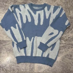 Blå och vit stickad tröja med mönster - Säljer en stickad tröja i blått och vitt med ett unikt, abstrakt mönster. Tröjan har rund halsringning, ribbade muddar och är långärmad. Perfekt för dig som gillar att sticka ut med coola detaljer och mjuka material.