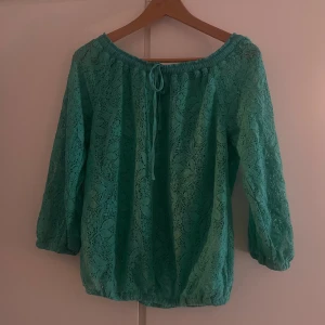 Turkos blus med knyt - turkos blus med spetsmönster och knytning vid halsen. Trekvartsärmar. 