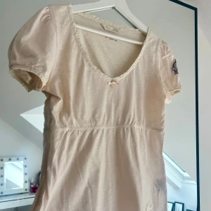 Ljusrosa topp från Odd Molly - Supersöt ljusrosa topp från Odd Molly, liten rosett framtill och spetskant runt halsen. Puffiga korta ärmar med broderad detalj på ena ärmen. Är lite gulaktig under armarna om man tittar noga. Vet ej om det går bort i tvätten.