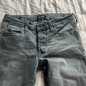 Grå jeans från Jack & Jones 28/32 slim Glenn - Säljer ett par snygga grå jeans från Jack & Jones. De har klassisk femficksdesign, normal passform och raka ben. Jeansen är i mjukt denimtyg och har bälteshällor och knappgylf. Perfekta för en chill och stilren look.
