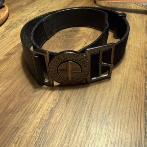 Svart Stone Island bälte - Snyggt svart bälte från Stone Island med bred design och ikoniskt metallspänne med logotyp.