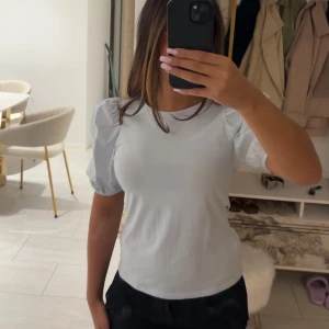 Ljusblå topp med puffärm från H&M - Supersöt ljusblå topp från H&M med korta puffärmar som ger en trendig siluett. T-shirten har rund halsringning och är gjord i mjuk bomull, perfekt för en chill och stilren look.