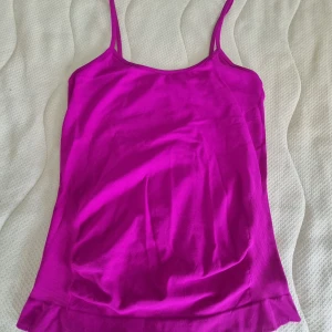  linnetopp med smala axelband  - Snygg fuchsiafärgad linnetopp med smala axelband och rak halsringning. Toppens material känns mjukt och stretchigt, perfekt för varma dagar. Enkel och stilren design som är lätt att matcha med jeans eller kjol.