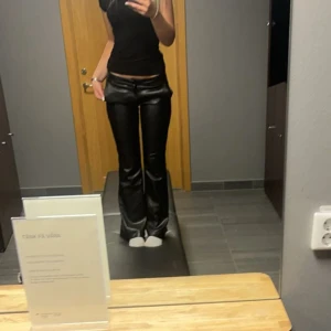 Svarta bootcut byxor i skinnimitation - Säljer ett par svarta byxor i skinnimitation med bootcut-modell. Byxorna har låg midja och sitter tajt upptill med utsvängda ben. Perfekta för dig som vill ha en edgy och trendig look.