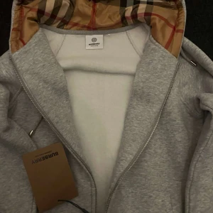 Ekta Grå hoodie från Burberry med huva - Jag säljer en ekta fin grå burberry hoodie, den är väldigt skön och fin för att använda. Plus har den tag. Jag säljer den på grund av att jag beställde fel storlek och den it passar mig. Pris kan man alltid diskutera, så oroa er it😁