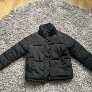 Svart pufferjacka från H&M - Svart pufferjacka från H&M med hög krage och tryckknappar och dragkedja framtill. Står mitt namn i men går enkelt att strecka över eller sätta namnlapp över så syns de inte! Inga hål eller fläckar 