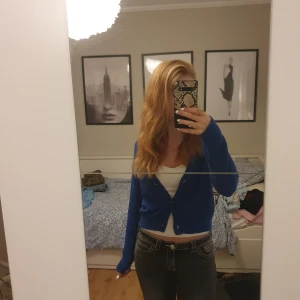 Blå stickad kofta med knappar - Säljer en blå stickad kofta från Lager 157 med v-ringning och tre bruna knappar framtill. Koftan är croppad och har långa ärmar samt ribbade muddar. Säljes då den inte kommer till användning!