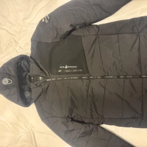 Svart pufferjacka Sail Racing M - Säljer en svart dunjacka från Sail Racing Patrol Jacket i storlek medium som är i fint skick. Jackan har huva, dragkedja framtill, bröstficka och sidfickor med dragkedja och snygga logodetaljer på både bröst och ärm. Perfekt för kalla dagar och har en clean, sportig look. Nytvättad och inte använt sedan dess. 
