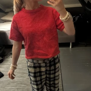 Röd stickad t-shirt med kort ärm - Säljer en röd stickad t-shirt med korta ärmar och rund hals. Tröjan har en mjuk och lite fluffig känsla, samt ribbad kant vid halsen. Passformen är normal och modellen är något croppad, perfekt för en chill och avslappnad stil.