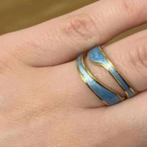 Blå och guldig vågig ring Rostfritt stål - Unik ring med vågformad design i blått och guld. Ringen har en öppen form och de blå partierna ramas in av tunna guldfärgade linjer. Perfekt för dig som vill sticka ut med ett färgglatt och trendigt smycke.