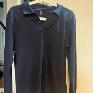 Mörkblå långärmad pikétröja C - Snygg mörkblå pikétröja från cubus i storlek 158/164. Tröjan har en krage, knäppning framtill och långa ärmar. Perfekt för en stilren look. Materialet känns mjukt och bekvämt mot huden.