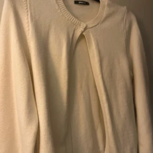 Vit kofta från Gina Tricot - aldrig använt  - Säljer en klassisk vit kofta från Gina Tricot i storlek S. Koftan har rund halsringning, lång ärm och stängs med en knapp upptill. Perfekt att slänga över en topp för en clean och enkel look.