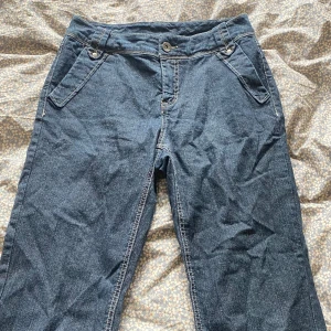 Mörkblå midwaist jeansbyxor med raka ben - Snygga mörkblå midwaist jeansbyxor med raka ben och klassiska fickor både fram och bak. Byxorna har tydliga kontrastsömmar och stängs med knapp och dragkedja. Perfekta för dig som gillar en enkel och tidlös stil.
