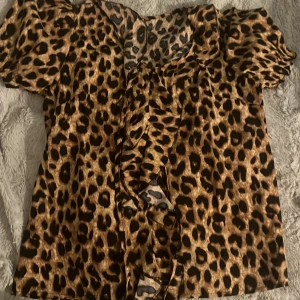 Leopardmönstrad blus med volang - Säljer en snygg blus med leopardmönster i bruna och svarta toner. Toppen har korta puffärmar och en volangdetalj framtill som ger extra attityd. Perfekt för dig som vill sticka ut med ett djurmönster och cool vibe.