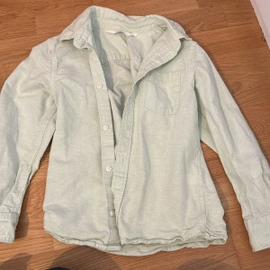 Ljusgrön bomullsskjorta med knappar - Snygg ljusgrön skjorta i bomull med klassisk krage och bröstficka. Skjortan har långa ärmar och stängs med vita knappar framtill. Perfekt att styla lager på lager eller bära som den är.