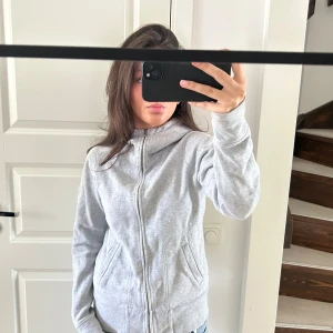 Grå hoodie  - Säljer en ljusgrå hoodie från Bikbok med dragkedja framtill och fickor på sidorna. Tröjan har huva och broderad logga på ryggen. Perfekt för en avslappnad stil.