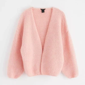 Ljusrosa stickad kofta från Lindex - Supermjuk och fluffig ljusrosa stickad kofta från Lindex. Koftan har en oversized passform, långa ärmar och är öppen framtill utan knäppning. Perfekt för lager-på-lager och ger en mysig känsla till din outfit.