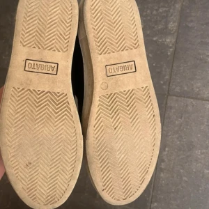 Svarta sneakers från ARIGATO - Säljer ett par svarta sneakers från ARIGATO med vit sula. Skorna har en klassisk och stilren design med rund tå och platt sula. Perfekta för dig som gillar minimalistisk stil och vill ha ett par bekväma vardagsskor. 