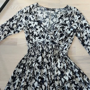 Svartvit omlottklänning från Bik Bok - Säljer en svartvit omlottklänning från Bik Bok med abstrakt mönster. Klänningen har trekvarts ärm, markerad midja med resår och v-ringad hals. Perfekt för dig som gillar en feminin och bekväm stil.