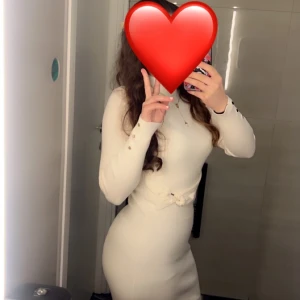 Vit långärmad tight klänning med gulddetalj - Säljer en elegant vit långärmad klänning med tight passform och hög hals. Klänningen har en söt gulddetalj i midjan och är perfekt för dig som gillar elegant stil.