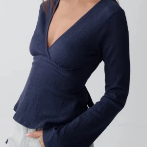 Mörkblå omlottopp med v-ringning - Snygg mörkblå omlottopp med djup v-ringning och långa ärmar. Toppen har knytband i midjan som ger en fin passform.
