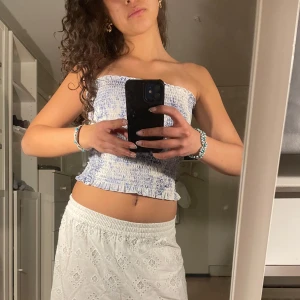 Blåvit smockad tubtopp - Säljer en söt tubtopp i blåvitt smockat tyg. Toppen är croppad och har en lätt volang nertill. Så fin till sommaren eller utomlands🧿🏝️