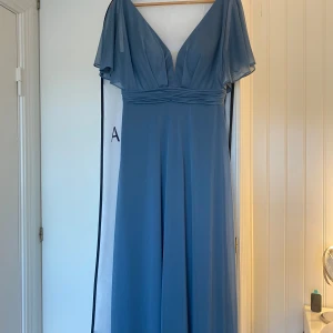  långklänning med v-ringning - Elegant blå långklänning med djup v-ringning och vida, korta ärmar. Klänningen har markerad midja med veckade detaljer och ett flytande fall. Perfekt för bal eller festliga tillfällen. Nypris är 1499kr💓