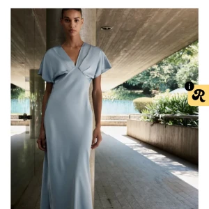 Populär Ljusblå långklänning med v-ringning - Elegant ljusblå långklänning med v-ringad omlott-topp och korta, vida ärmar. Klänningen har en mjuk, flytande siluett och är perfekt för speciella tillfällen. Snygg och stilren design som ger en exklusiv känsla. Klänningen är slutsåld i storleken på hemsidan och har prislapp kvar, endast testat. Pris kan diskuteras