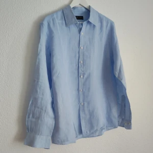 Ljusblå linneskjorta från Brooks Brothers - Säljer en klassisk ljusblå skjorta i linne från Brooks Brothers. Skjortan har lång ärm, knappar framtill och en tidlös krage. Perfekt för en stilren och avslappnad look.