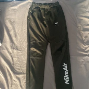 Svarta Nike Air mjukisbyxor - Säljer ett par svarta mjukisbyxor från Nike Air med vit logga längs benet och broderad Nike Air-detalj vid fickan. Byxorna har resår i midjan och är i standard fit, perfekta för en sportig look.